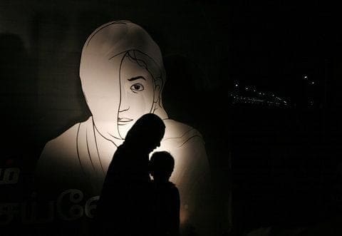 A woman walking past a billboard, with her child, during a candlelight vigil on the eve of International Women's Day in Chennai, Tamil Nadu.